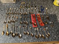 Full collection of souvenir spoons, two forks, and page marker arranged on countertop showing size, design variation, and quantity.