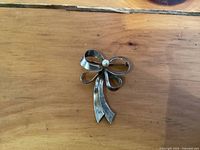 Front view of the sterling silver bow shaped brooch with central round pearl accent, showing tarnish and wear.