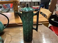 Tall pottery coffee pot with dark green and black circular pattern on table
