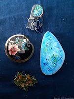 Image of three enameled pins and one scarf brooch arranged on fabric background.