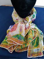 Scarf tied around a black mannequin neck showing the colorful design and the Basile label in the corner