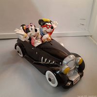 Angled side view of ceramic Mickey and Minnie Mouse in convertible car music box showing characters waving and car details.