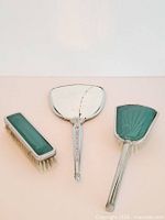 Hand mirror, long brush, short brush displayed front side; shows cracked mirror and green enamel backs