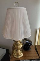 Brass table lamp with white pleated shade beside black spotlight