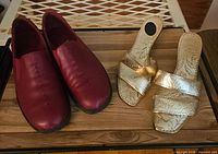 Red loafers and gold sandals side by side on wooden surface