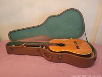 Guitar in open hard case showing spruce top and accessories