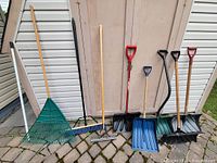 Front view of all seven yard tools leaning against shed