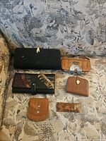 All six items arranged on couch: two long wallets, vinyl card case, two coin purses, tortoiseshell barrette