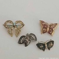 Group shot showing all four brooches: bow, pink butterfly, leaf cluster, black butterfly