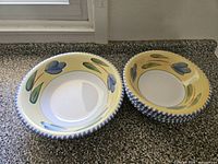 Two stacked ceramic bowls showing yellow glaze, blue tulip motif, white well, blue-checked rim
