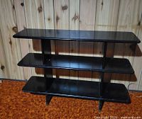 Front view of three-tier black shelf against wood panel wall