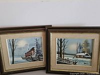 Both framed winter landscape paintings side-by-side