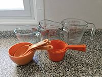 Front view of three Pyrex glass measuring cups and nested orange plastic measuring cups