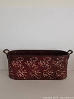 Front view showing burgundy color, gold scroll pattern, oval shape and both handles