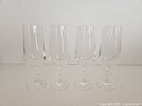 Four clear crystal champagne flutes standing side by side, showing bowls, faceted stems with decorative knops, and round bases