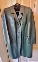 Front view of green leather coat hanging on hanger showing collar, button closure, long sleeves