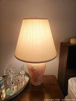 Lamp illuminated showing ceramic floral base and pleated shade