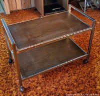 Full view of two-shelf utility cart showing veneer shelves, metal frame, handles and casters