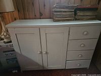 Full front view of cabinet showing two doors left, four drawers right, white painted finish