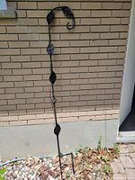 Full view of black wrought iron garden stake standing against brick wall