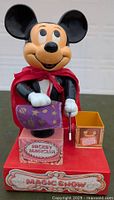 Front view of 1976 Durham Mickey Magician Magic Show toy showing Mickey Mouse figure, red cape, purple cloth, magic wand, and decorative base with 'Magic Show' label.