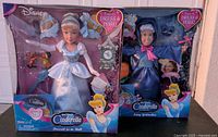 Front view of unopened Cinderella and Fairy Godmother dolls in original boxes showing accessories and packaging details.