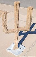 Cactus shaped cat pole with two upward arms covered in beige carpet material on a square base covered with a blue towel. View from left side.