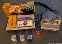 Kodak Instamatic 124 camera in box with manual, Polaroid Impulse instant camera, and 35mm film roll arranged on surface