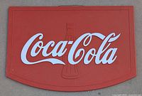 Close-up front view of Coca-Cola plastic sign with embossed bottle and white logo on red background