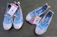 Front angle of the two pairs of silver glitter Mary Jane children's shoes, showing size 12 tags and Disney Princess soles