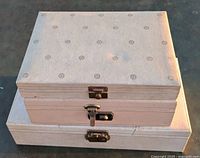 Three stacked cream jewelry boxes with circular prints and metal clasps on a concrete floor.