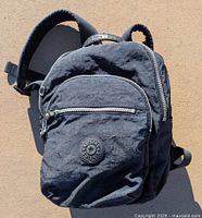 Front view of black Kipling nylon backpack showing front zip pocket and logo patch.