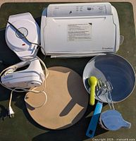 Photo showing FoodSaver V2830 vacuum sealer, electric hand beaters, Pampered Chef pizza stone, mixing bowl, lemon squeezer, and whisk attachment viewed from above on a surface.