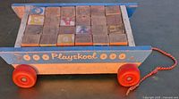Side view of Playskool wooden pull-along wagon loaded with 24 wooden letter blocks showing wear and faded colors.