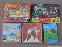 Overview photo showing all five items in the lot, two board games and three puzzles, all Simpsons themed.