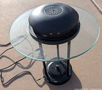 Top view of the lamp showing clear circular glass shade with black metal base beneath, vented top and power cord extending outward.