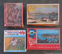Four vintage jigsaw puzzle boxes seen from above showing front artwork and titles including religious scene, harbor boats, coastal town, and a child in garden