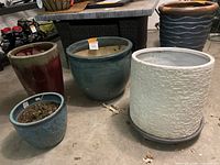 Four ceramic planters arranged on floor showing different colors and sizes