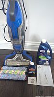 Front view of Bissell CrossWave cleaner with brush rolls, cleaning formulas, and manual.