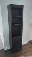Front view of the tall dark wood Pottery Barn bookcase showing two open shelves, pullout shelf, and closed lower cabinet with door and knob.