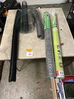 Top-down view of multiple rolled garden netting materials and cages on a table including black weed cloth, green netting, poultry wire and chicken wire.