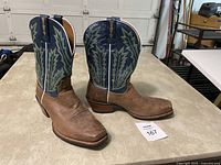 Front and side view showing brown leather foot and blue upper with green stitched design, square toe and pull straps