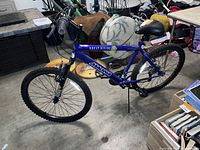 Side view of Magna Great Divide mountain bike showing blue frame, knobby tires, padded saddle, and handlebar with gear shifters.