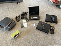 Full lot showing Sony portable DVD player open with 9-inch screen, two Sony Blu-ray players with remotes and power adapters, green travel alarm clock, black Cherry carrying case, and associated cables.