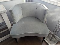 Full view of the grey/light blue curved velvet chair showing button tufted back and rounded seat cushion.