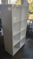 Photo showing full height view of white Ikea Kallax shelf unit standing upright. Shows clean white rectangular frame with 8 cubbies arranged in 2 columns and 4 rows.