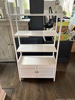 Front view of white four-shelf bookshelf with bottom cabinet doors on hardwood floor.