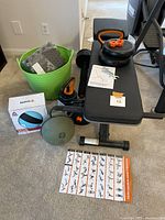 Overall lot view showing adjustable weight bench, dumbbells, medicine balls, floor mats in green tub, and instructional guides.