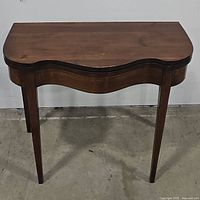 Front view of the antique fold over game table showing scalloped edge and wood finish.