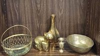 Wide shot showing all six brass items arranged - basket, cat figurine, ribbed vase, narrow vase, small candlestick, and bowl.